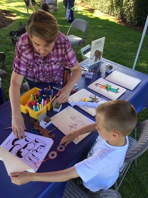 A Museum volunteer helps a child make a paper puppet.