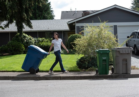 Resident on sidewalk with recycling cart at house