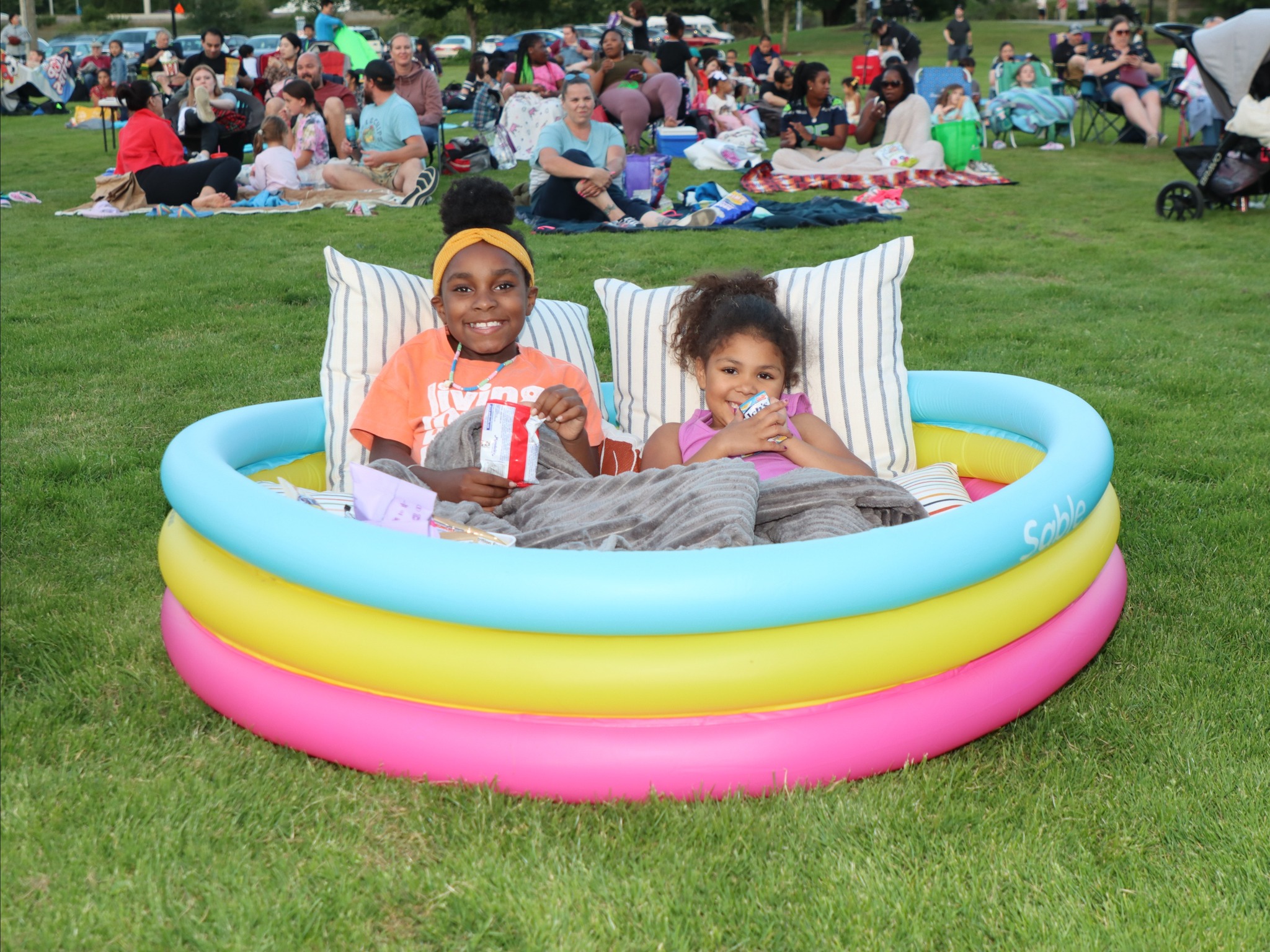 Two kids in an inflatable pool filled with blankets and pillows at park. 